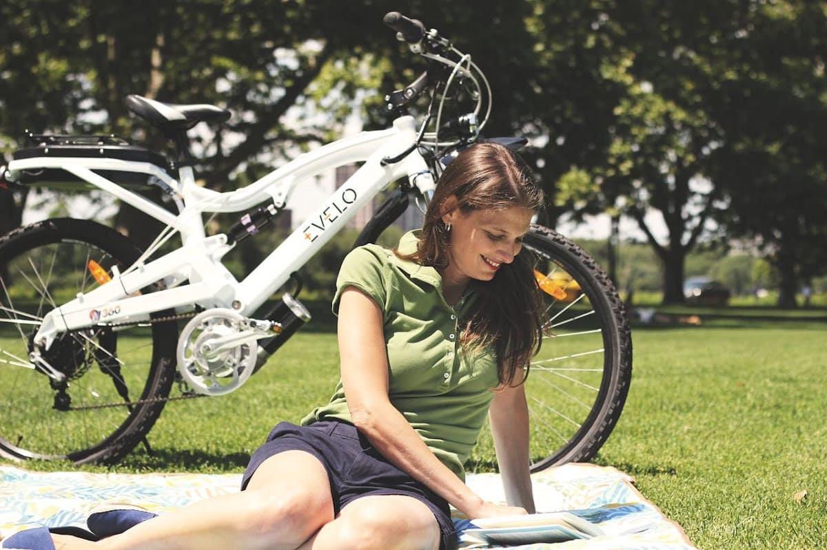 Eine Frau sitzt auf einer Decke auf der Wiese, hinter ihr ein e-Bike